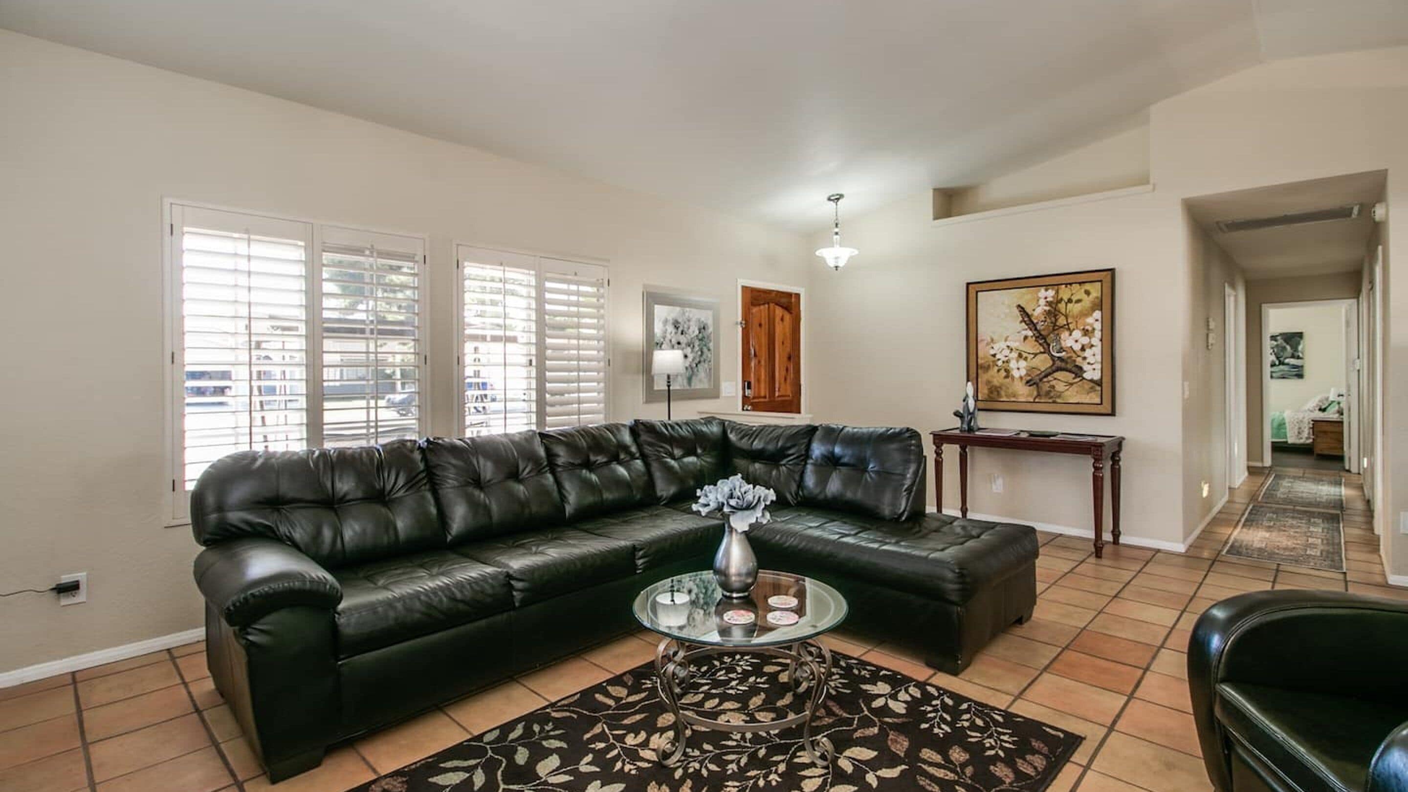 A living room with a black leather sofa, a glass coffee table with a vase, and a patterned rug.