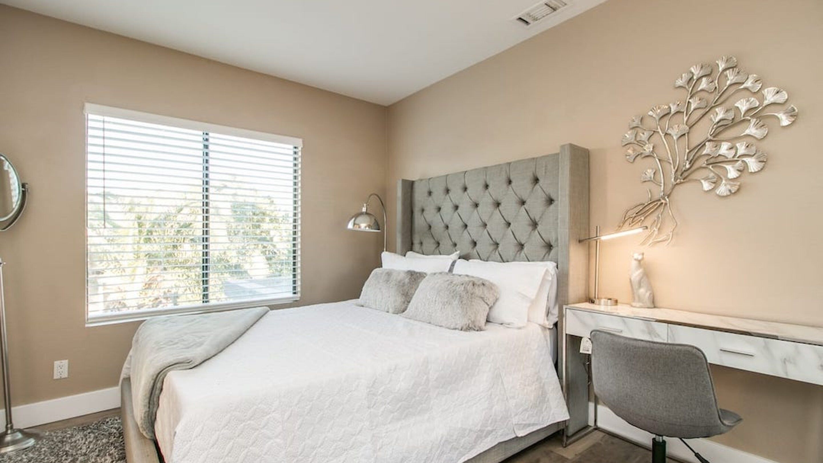 Een slaapkamer met een gebonden hoofdbord, een bed met witte lakens, een nachtkastje met een lamp en een decoratief wandobject.
