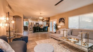 A modern living room with a sofa, ottomans, and a coffee table. There is a kitchen in the background with a dining area. - Amazing Remodeled Scottsdale 5 Bdrm W/pool! (Scottsdale)