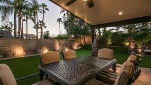 An outdoor patio with a table and chairs, surrounded by a well-maintained lawn and palm trees. - Amazing Remodeled Scottsdale 5 Bdrm W/pool! (Scottsdale)
