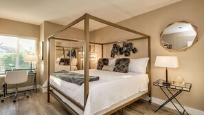 A four-poster bed with a white bedspread, a desk with a chair, a round mirror, and a lamp on a side table. - Amazing Remodeled Scottsdale 5 Bdrm W/pool! (Scottsdale)