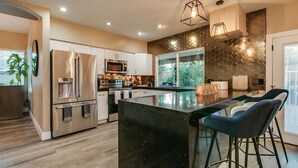 A modern kitchen with stainless steel appliances, a large island with bar stools, and a hexagonal patterned backsplash. - Amazing Remodeled Scottsdale 5 Bdrm W/pool! (Scottsdale)