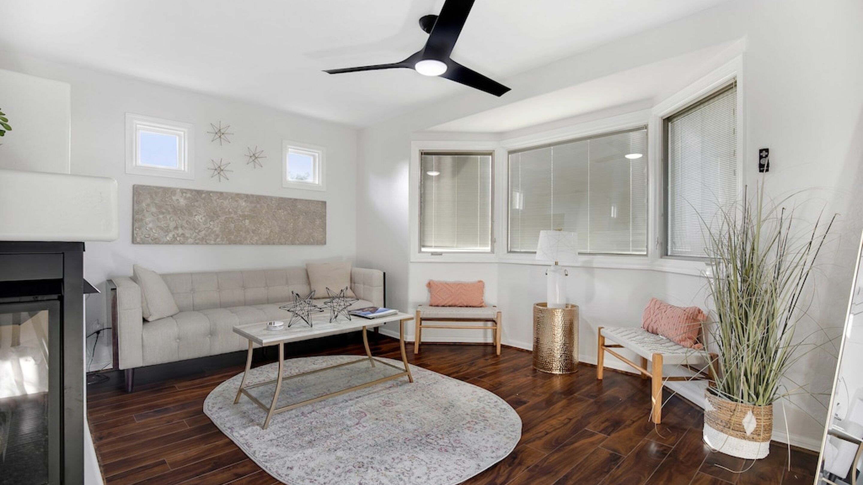 A modern living room with a fireplace, a ceiling fan, and a large window providing natural light.