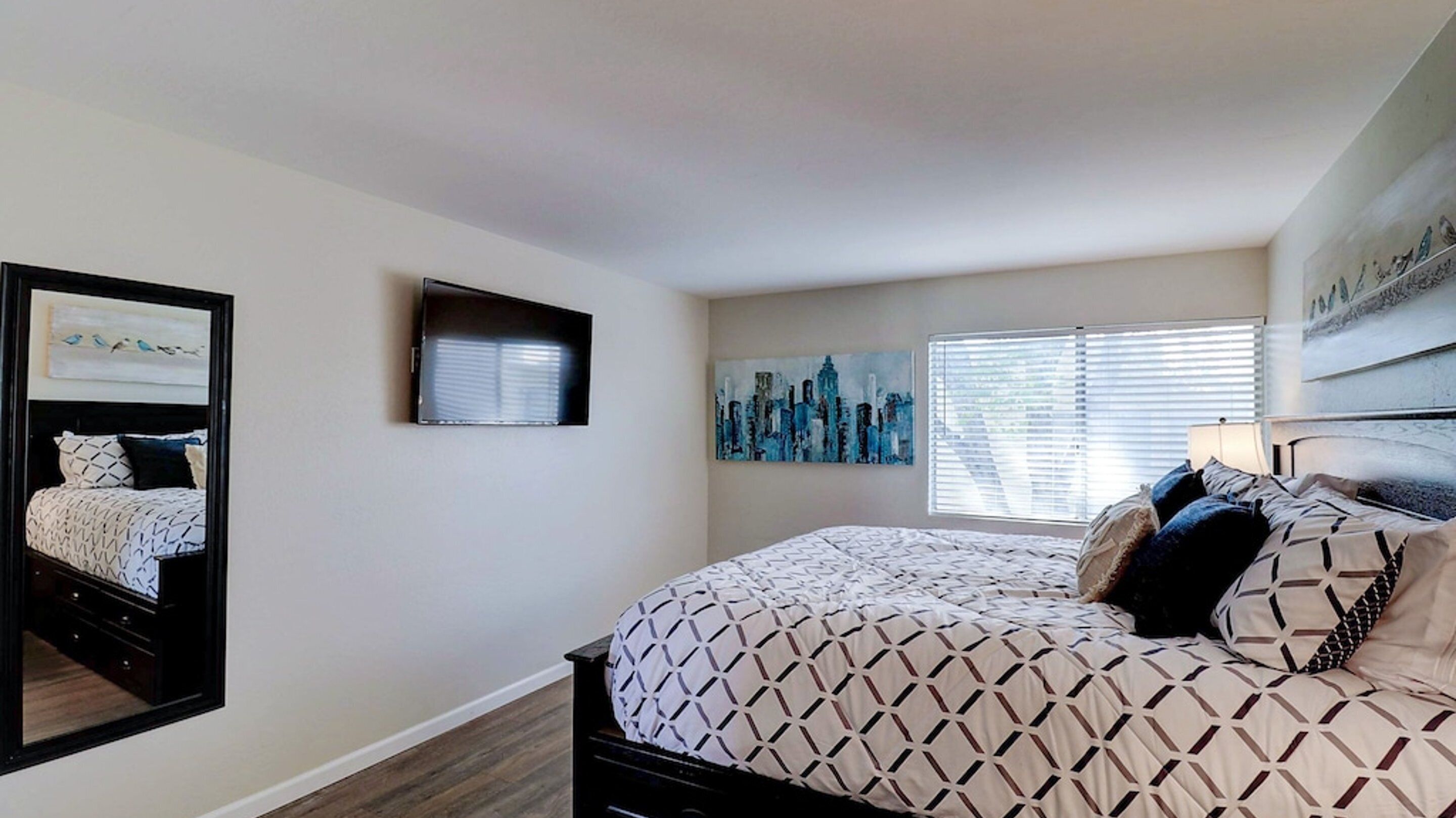 A bedroom with a bed, a dresser, a mirror, and artwork on the walls.