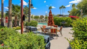 Un espace extérieur aménagé en terrasse, avec une piscine, des palmiers et un barbecue.