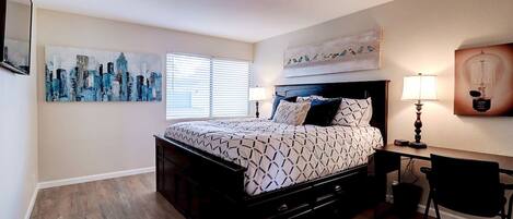 A bedroom with a bed, a desk, a chair, a lamp, and artwork on the walls.