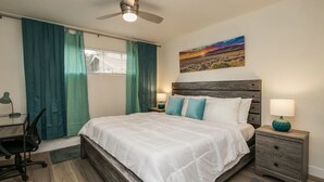 A bedroom with a bed, a desk, a chair, a nightstand, a lamp, and a painting on the wall. - Remodeled 2 Bdrm w/ Yard in Old Town Scottsdale! (Scottsdale)