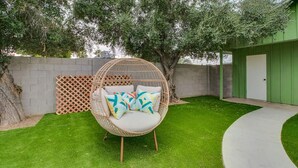 A round wicker chair with cushions on a well-maintained lawn, a wooden fence, and a green building in the background. - Remodeled 2 Bdrm w/ Yard in Old Town Scottsdale! (Scottsdale)