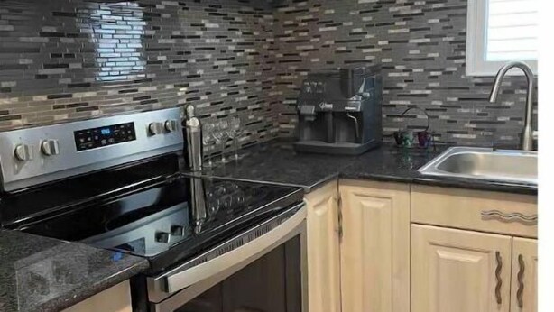 A modern kitchen with a black stove, a coffee maker, and a sink.