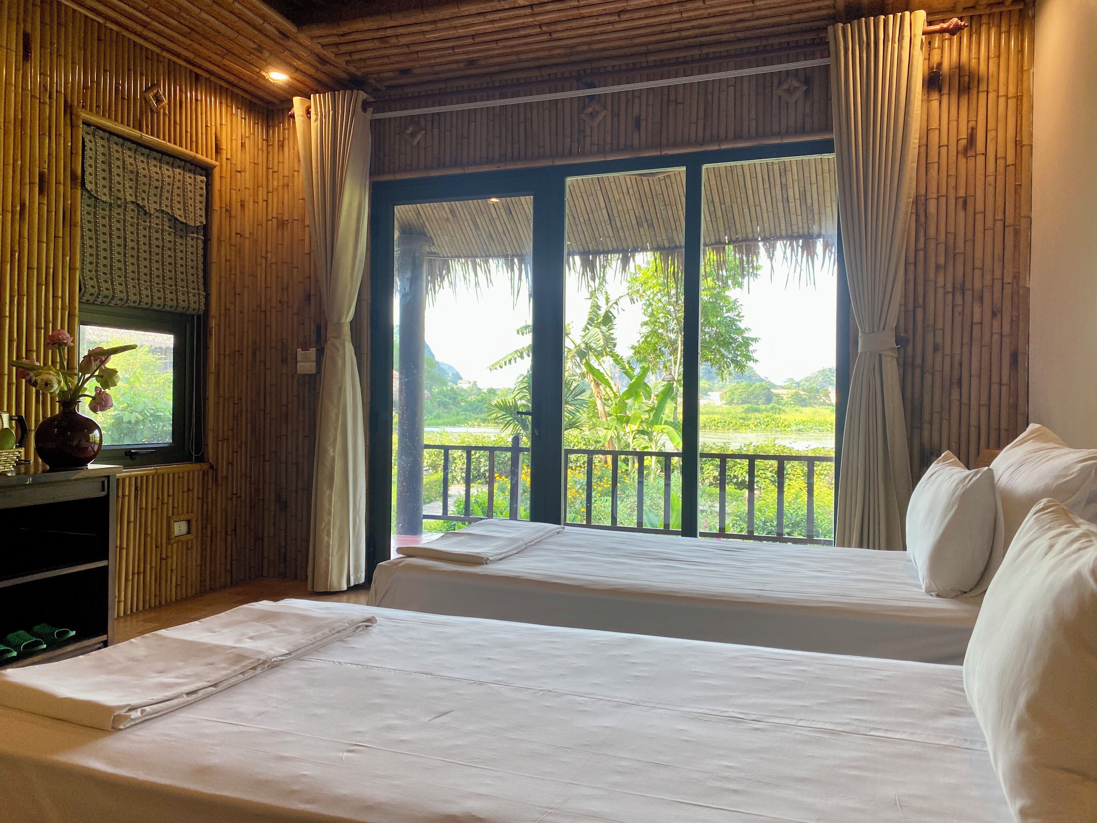 A room with two beds, a TV, and a view of a lush garden.
