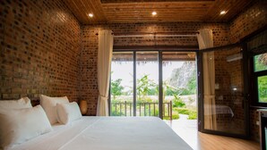Un dormitorio con una cama grande, una pared de ladrillo y vistas al verdor exterior.