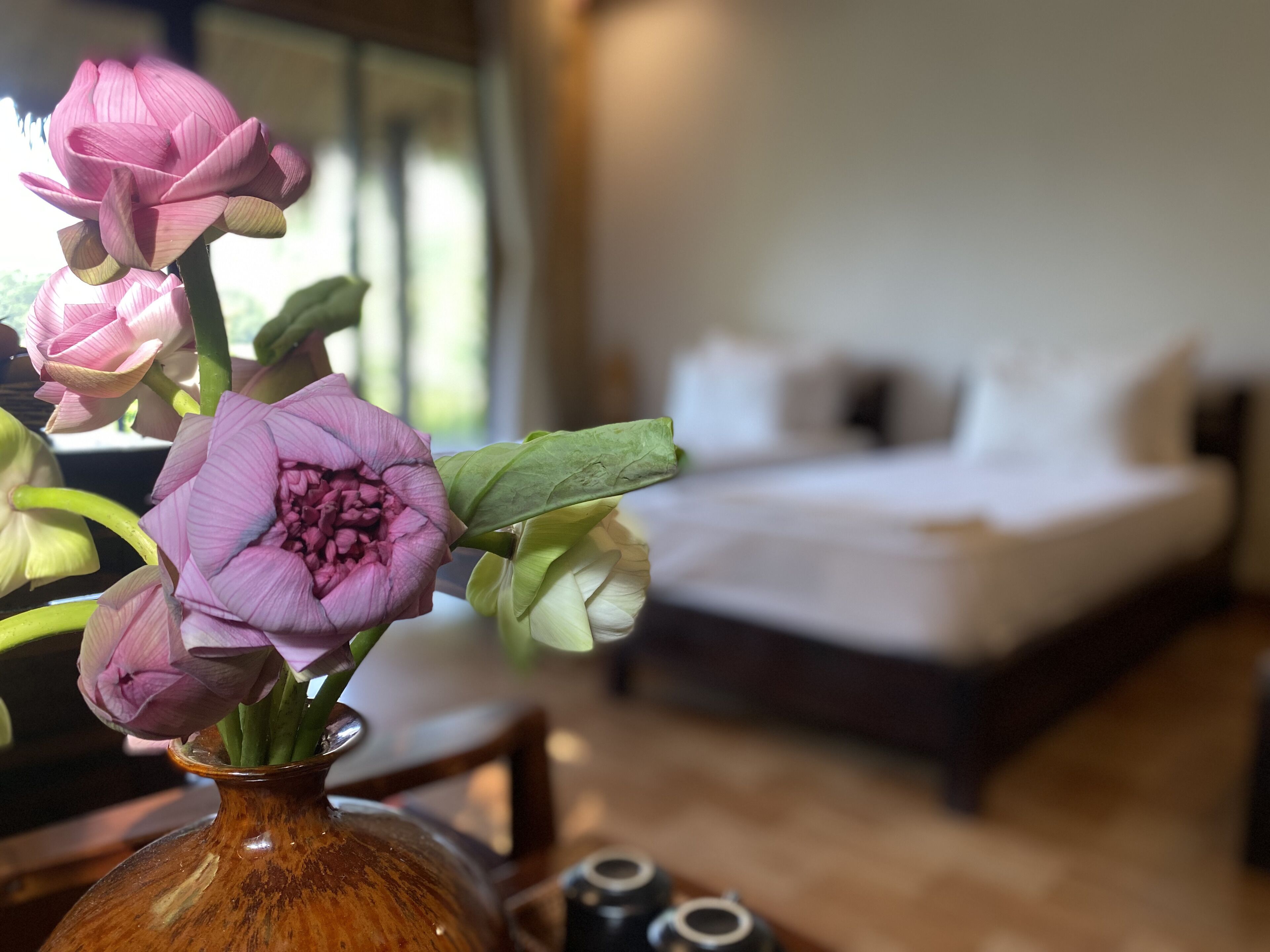 Un dormitorio con cama, un florero con flores y una ventana.