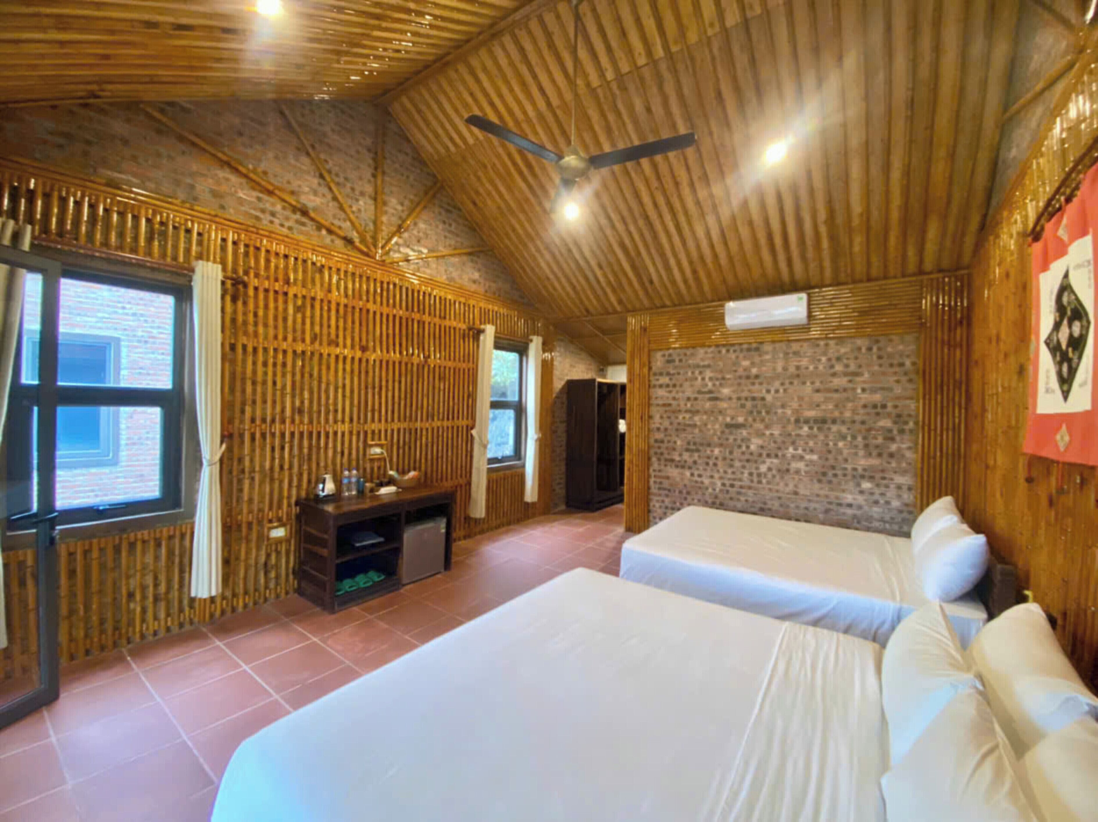 Quarto com duas camas, teto de madeira, parede de tijolo e uma janela.