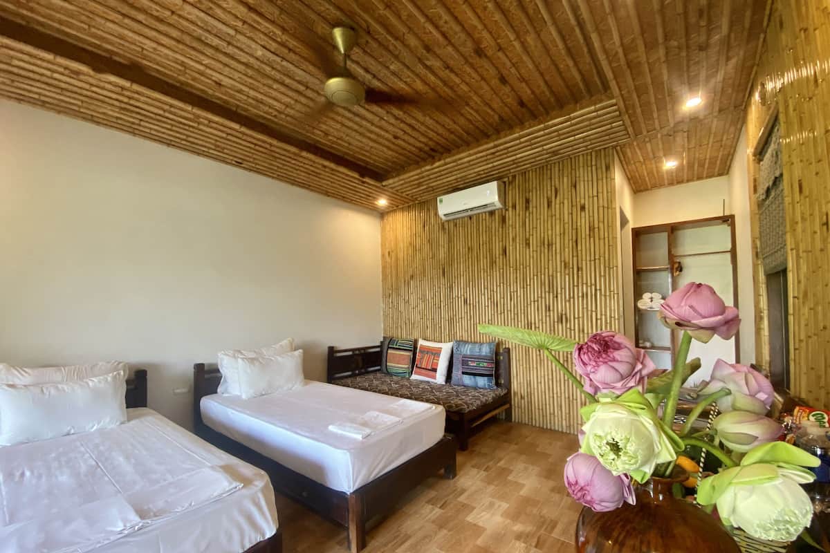 A hotel room with two beds, a wooden ceiling, a wall-mounted air conditioner, and a vase with flowers.