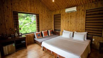 A wooden room with a large bed, a small table, and a window with a view of greenery.