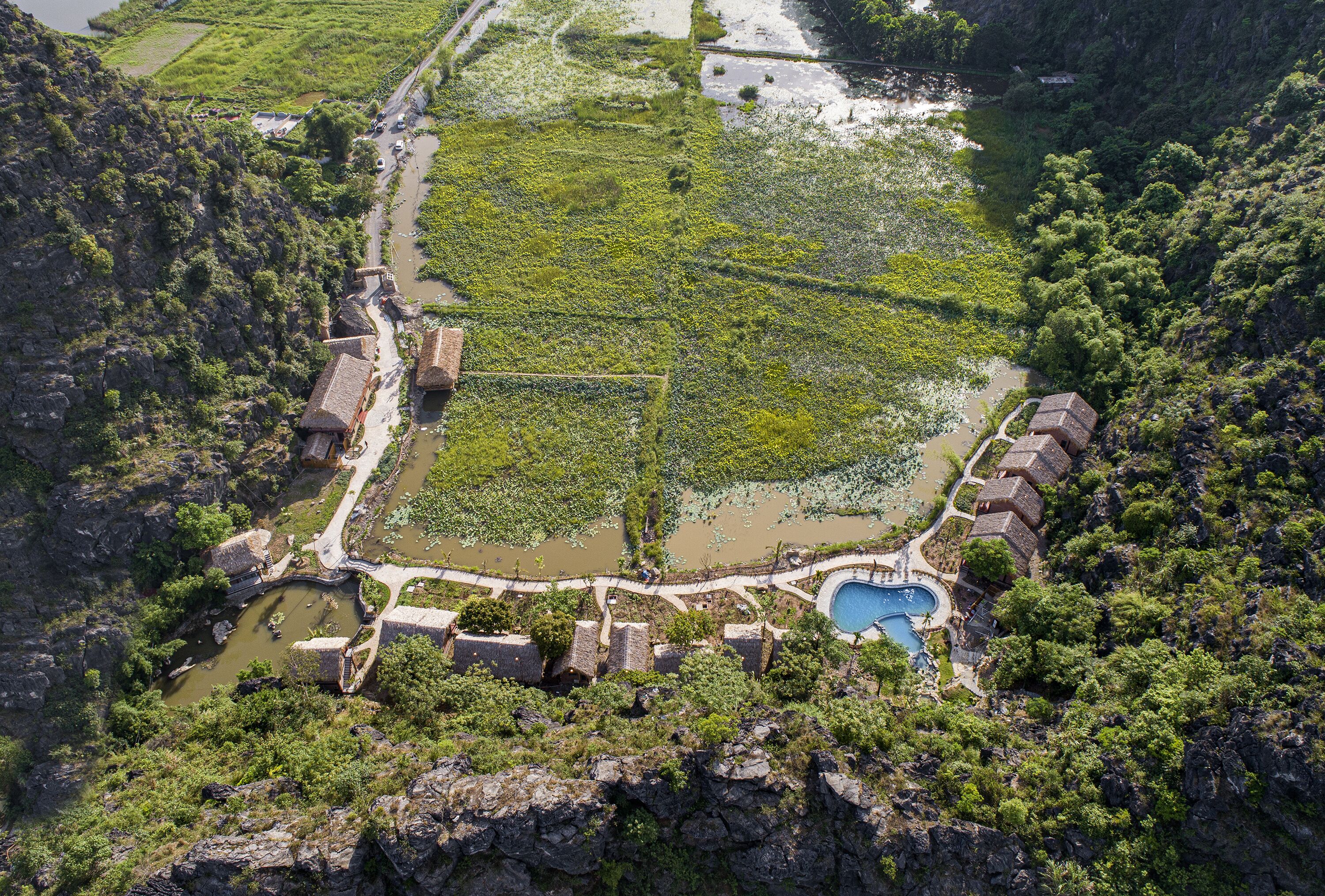 An aerial view of a traditional village with terraced fields, a central water body, and stone buildings.