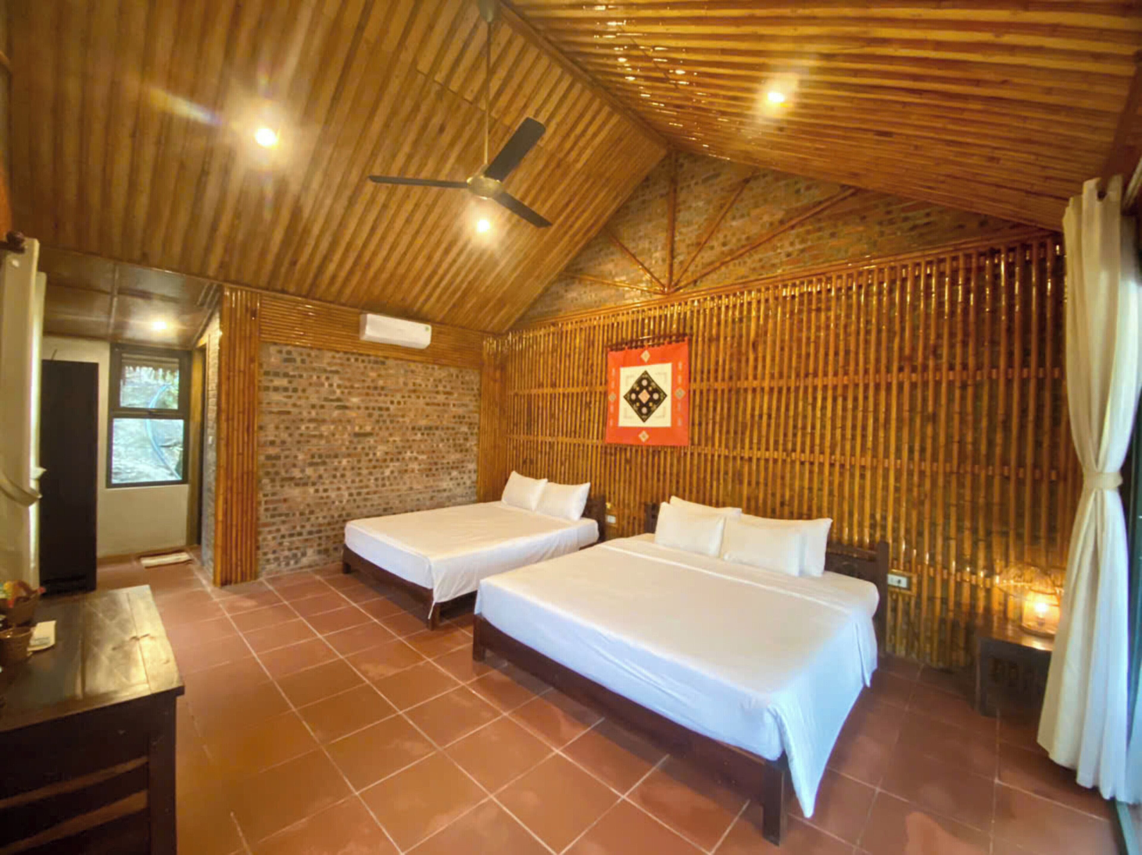 Una habitación con dos camas, techo de madera, pared de ladrillo y una ventana.