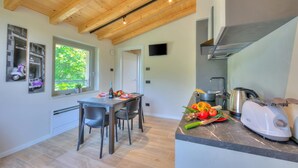 A modern kitchen with a wooden ceiling, a dining area with chairs, a window with a view, and a kitchen counter with a kettle and a toaster. - Ricomilla-Ulivo -Balcony, Garden & Privat, Roè Volciano, Italy (Roè Volciano)