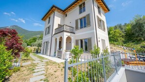 A two-story house with a balcony, a stone pathway, and a fenced garden area. - Ricomilla-Ulivo -Balcony, Garden & Privat, Roè Volciano, Italy (Roè Volciano)