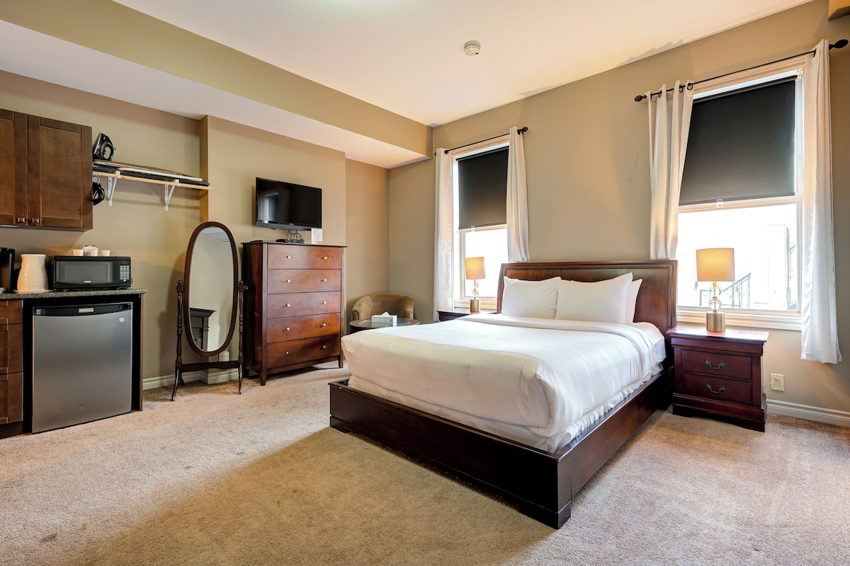A bedroom with a bed, dresser, vanity, and a television.