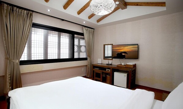 Une chambre d’hôtel avec un lit, un bureau équipé d’un ordinateur, un petit réfrigérateur et une grande fenêtre avec des rideaux.