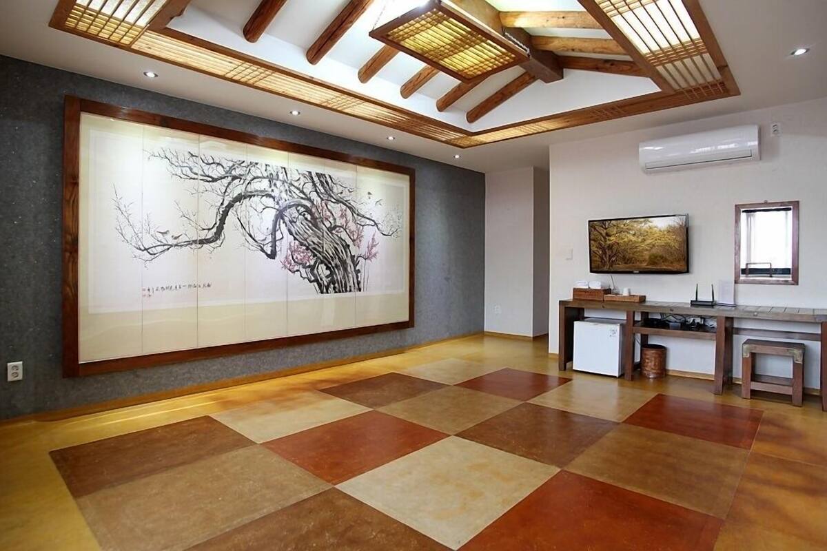 Una habitación espaciosa con un amplio cuadro abstracto en la pared, una consola de madera con un televisor de pantalla plana y un diseño moderno de techo.