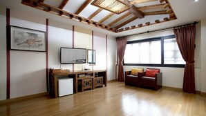 Habitació amb sostre de fusta, televisor sobre un suport de fusta, nevera petita, armari de fusta, finestra amb cortines i sofà amb coixins.