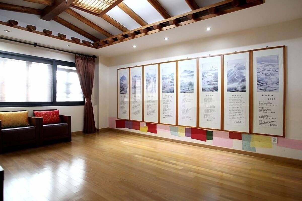 Una habitación con suelo de madera, un sofá con cojines, una ventana con cortinas y una pared decorada con cuadros y texto.