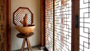 Una habitació japonesa tradicional amb una porta corredissa de fusta, una finestra decorativa d'octàgon i un gran bol de ceràmica sobre un pedestal de fusta.