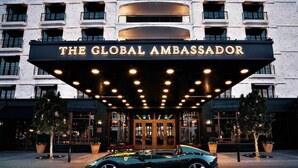 En byggnad med en stor, upplyst skylt som visar texten ”THE GLOBAL AMBASSADOR”, och en parkerad cabriolet framför.