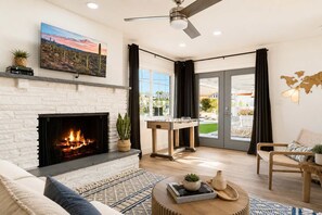 A living room with a fireplace, a sofa, a coffee table, a foosball table, and a view through a glass door.