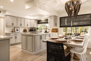A modern kitchen with white cabinetry, a central island, and a dining area set for six. - Villa w/heated pool & spa (Phoenix)