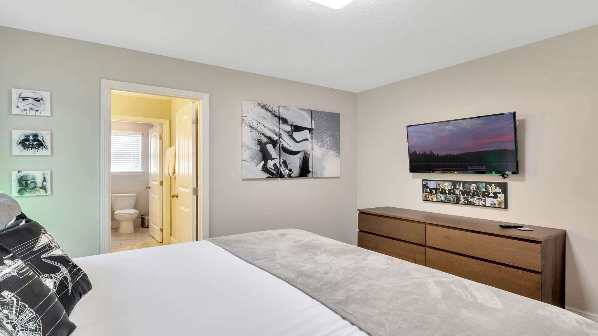 A bedroom with a bed, a dresser, a TV, and Star Wars-themed artwork.