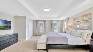 Une chambre à coucher avec un grand lit, une table de chevet, une télévision, une commode et un tableau au mur.
