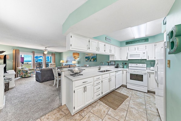 A spacious kitchen with white cabinets, a central island, and a view of the outside. - Gulf View Paradise – Private Beach Access, pool and tennis/pickle ball court! (Gulf Shores)