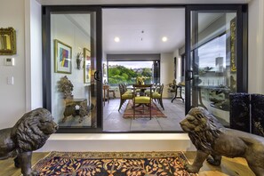 A modern interior with a glass door leading to a dining area, a lion statue, and a view of greenery outside. - The Address (Napier)