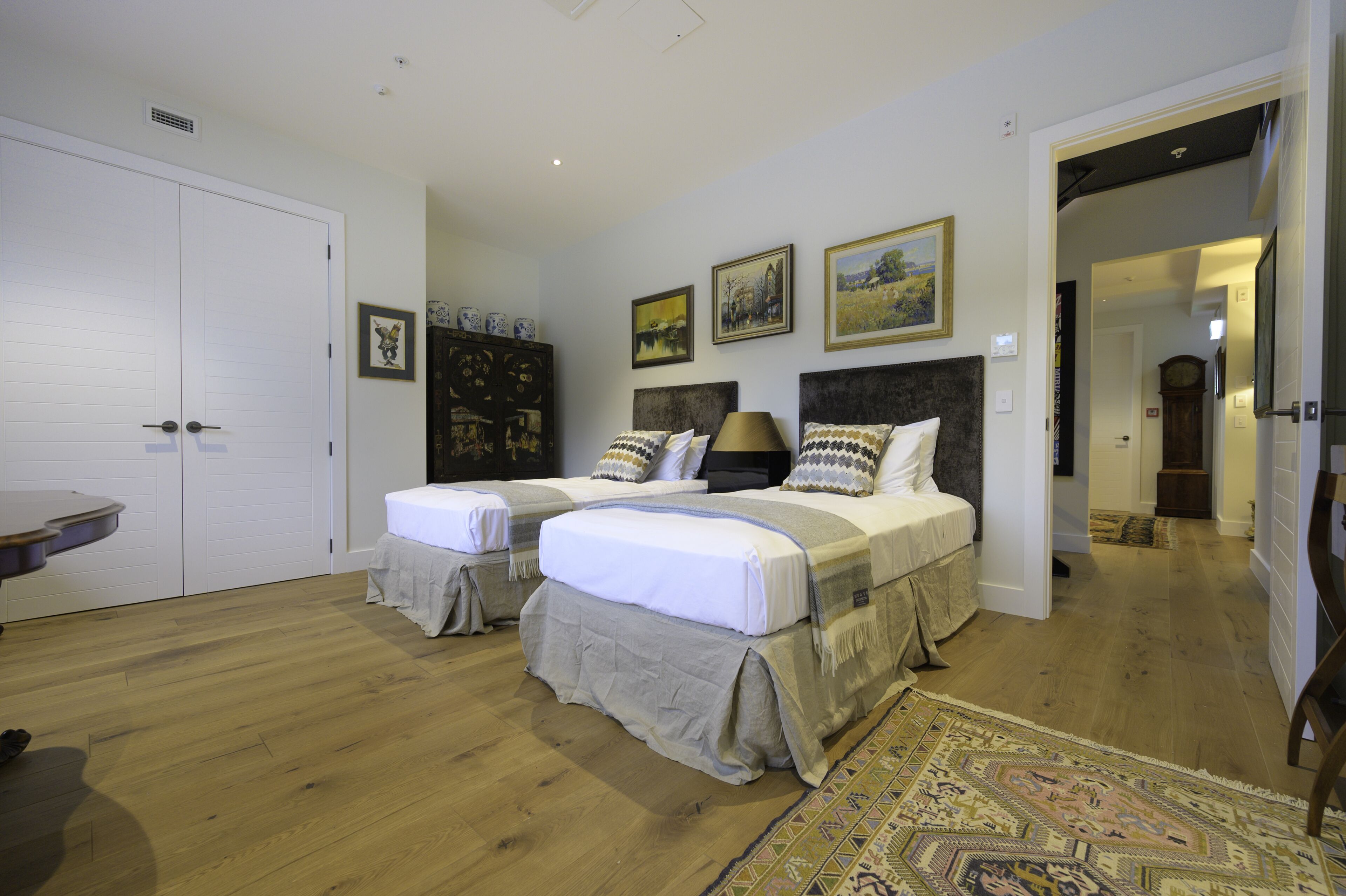 Un dormitorio con dos camas, piso de madera, un espejo grande y un armario.