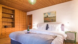 Un dormitorio con una cama grande, una estantería de madera, un cuadro en la pared y una mesita de noche con una lámpara.