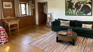 Un salón acogedor con pisos de madera, un sofá verde, una mesita de centro y un cuadro de vacas.