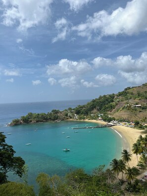 A coastal landscape with a beach, boats, and a hilly backdrop. - Reefside Villa Tobago (Bon Accord)