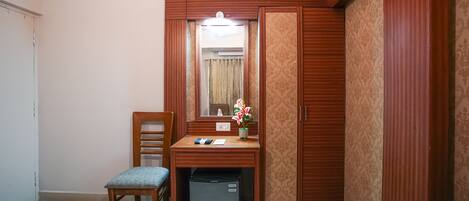 A compact room with a wooden desk, a chair, a small refrigerator, and a mirror.