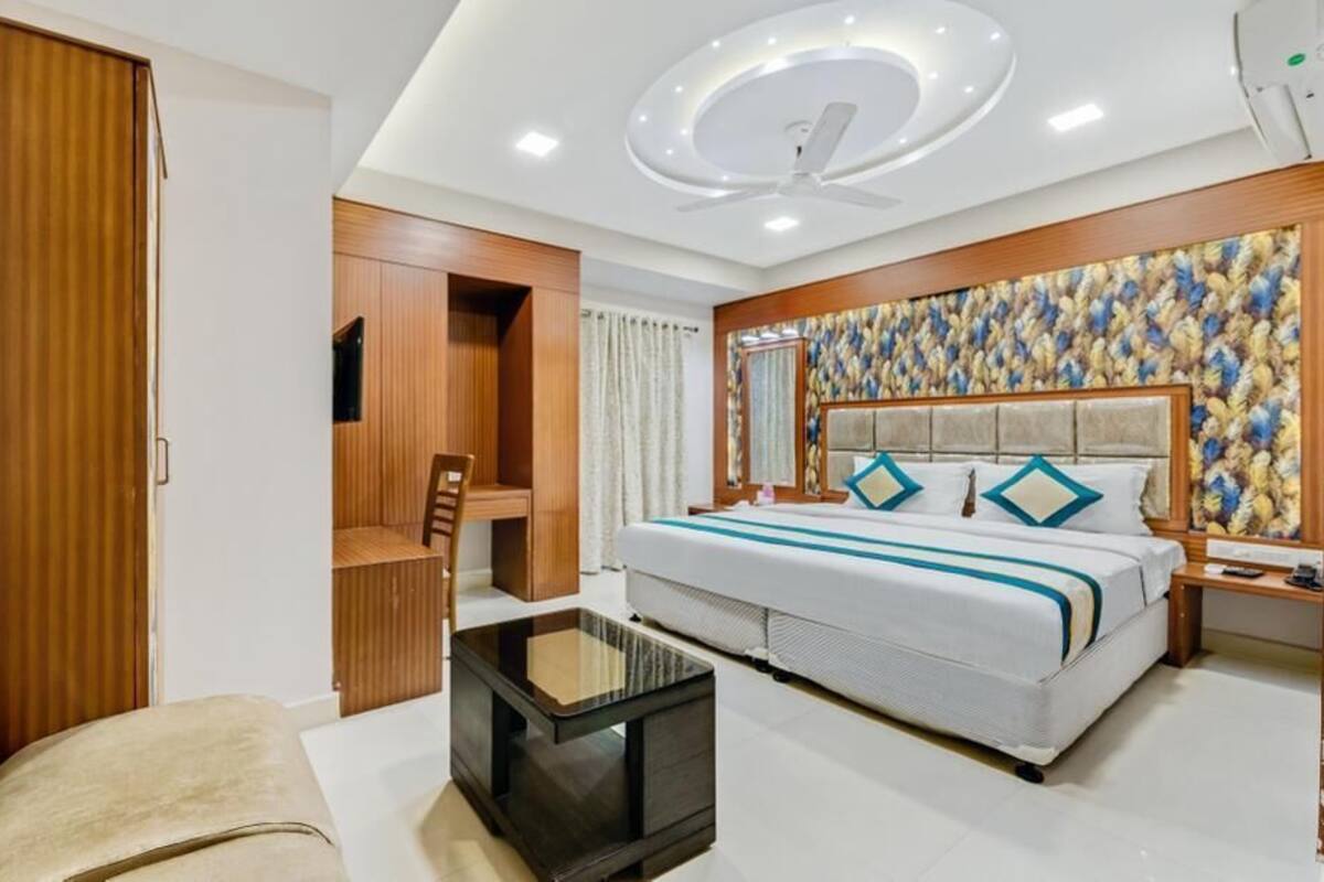 A modern hotel room with a large bed, a desk, a chair, and a small table.