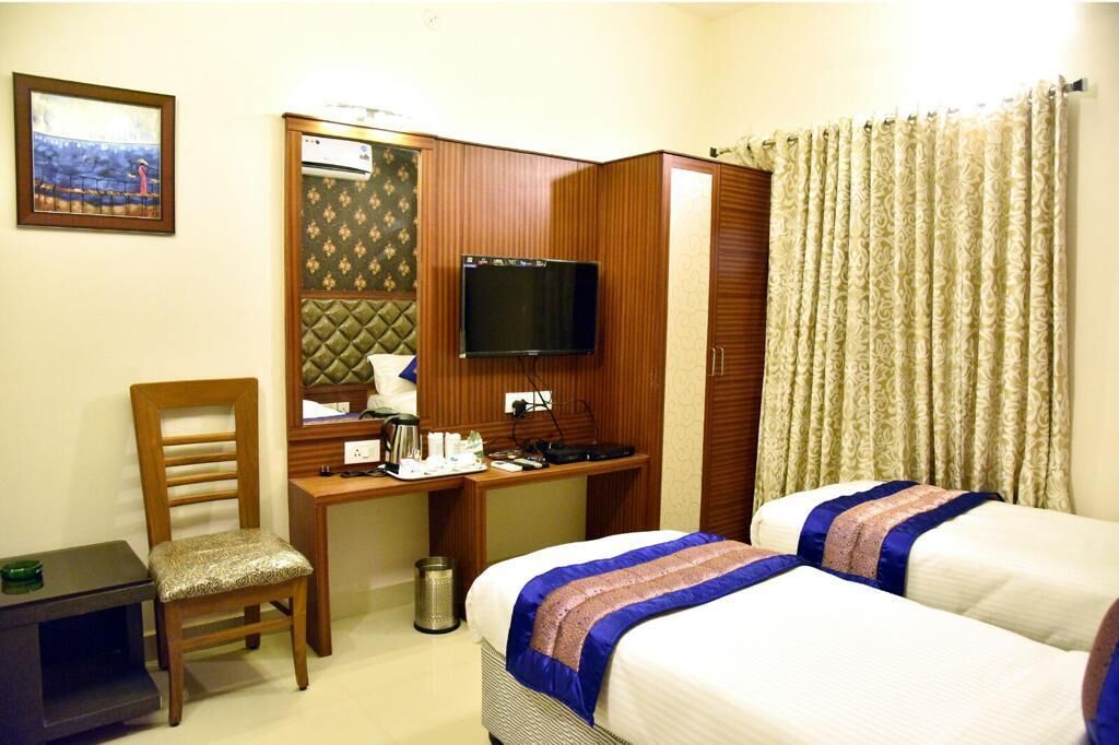 A hotel room with a bed, a desk with a television, a chair, and a window with curtains.