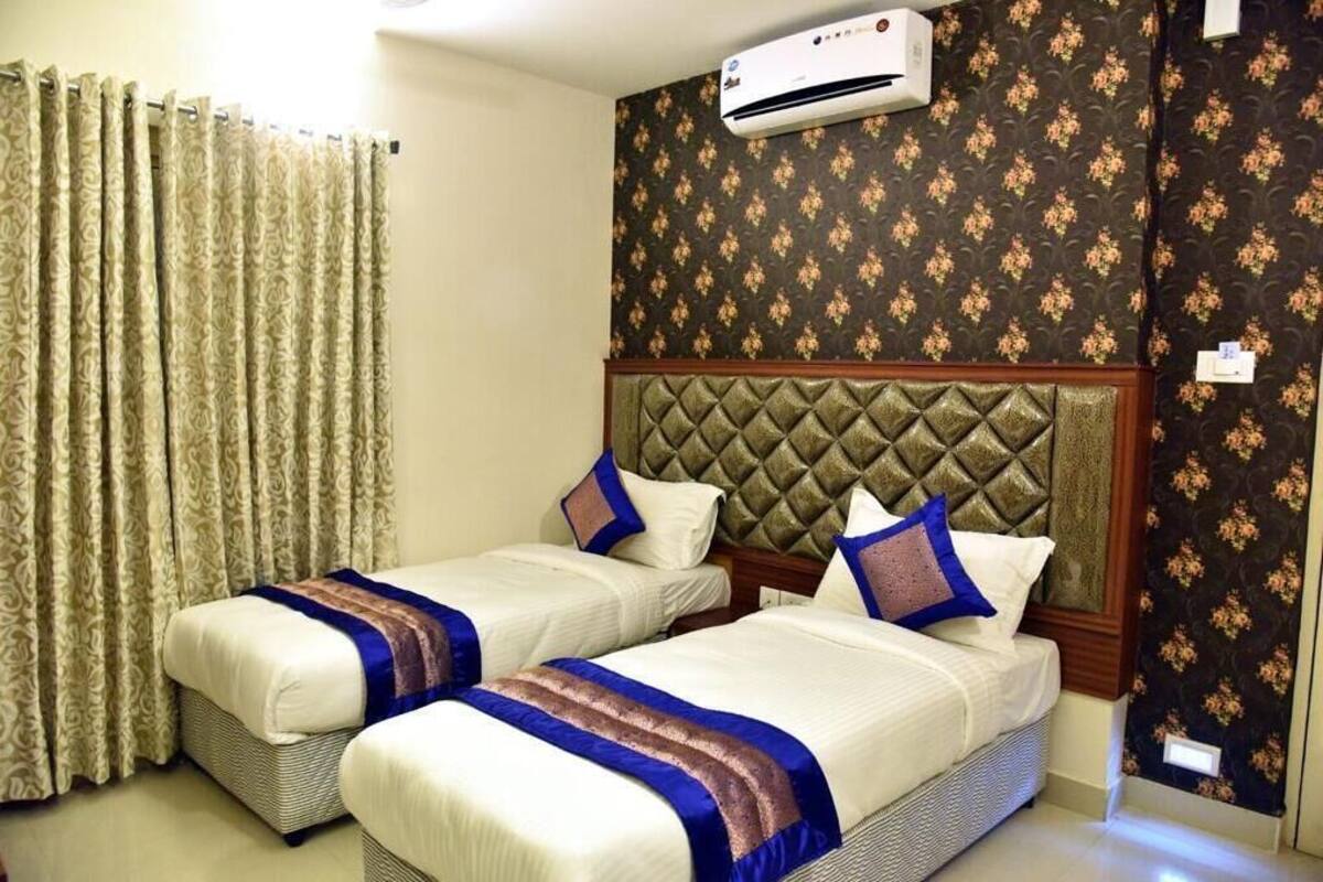 A hotel room with two beds, a patterned wall, and an air conditioning unit.