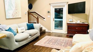 A living room with a sofa, a patterned rug, a television, and a staircase. - Best of Tides - Make family memories! (Galveston)