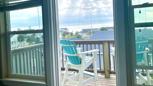 A view from a window with a wooden deck, a turquoise chair, and a view of the water and houses in the background. - Best of Tides - Make family memories! (Galveston)