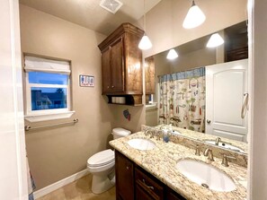 A bathroom with two sinks, a toilet, a window, and a mirror. - Best of Tides - Make family memories! (Galveston)