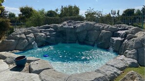 Een hottub omringd door grote rotsen en een helderblauw zwembad.