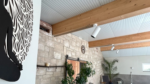 Ein Innenhof mit Steinwand, Holzbalken, einer hängenden Pflanze und Sitzmöbeln.