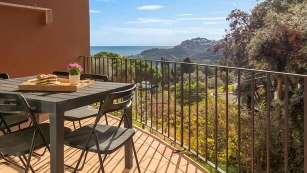 Een balkon met een tafel en stoelen, met uitzicht op een prachtig landschap met bomen en de zee.